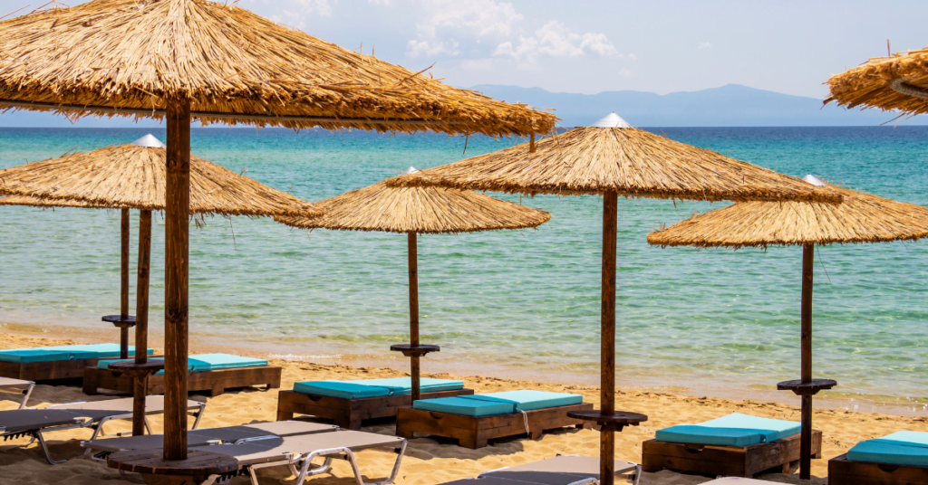 kiezelstrand met ligbedden en rieten parasols en blauwe zee